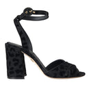 A pair of black leopard print suede ankle strap heels sandals with a leather buckle closure.
