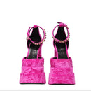 Pair of pink high-heeled shoes with embellishments on a white background